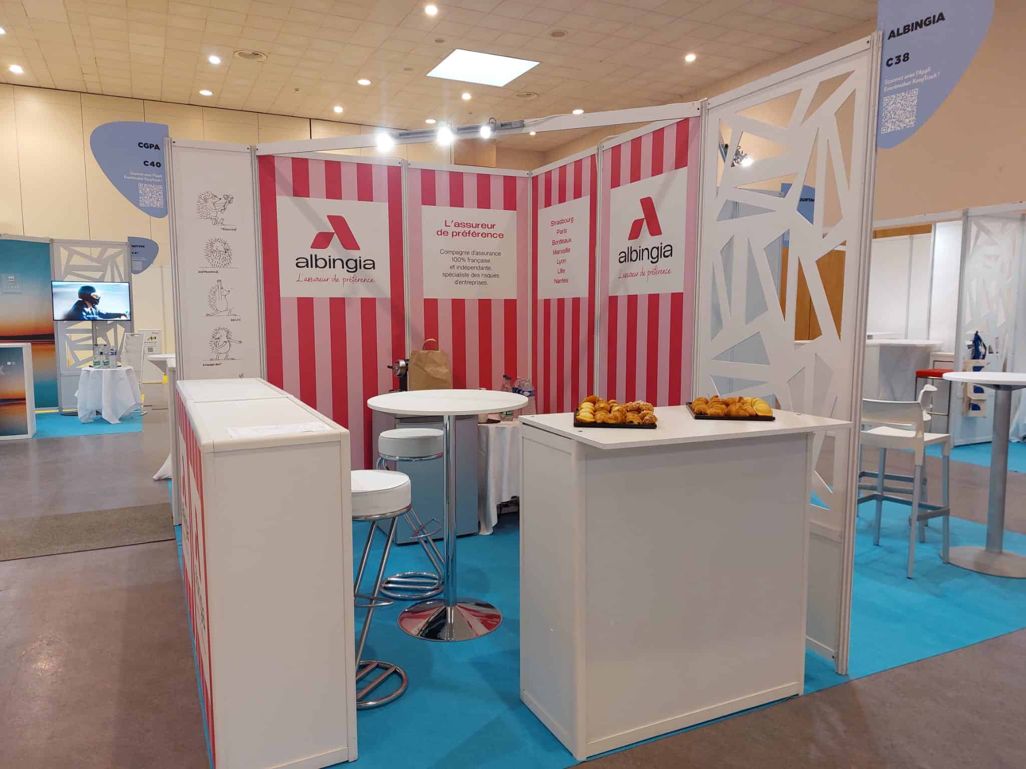 Albingia insurance booth at a trade fair with seating and promotional materials.