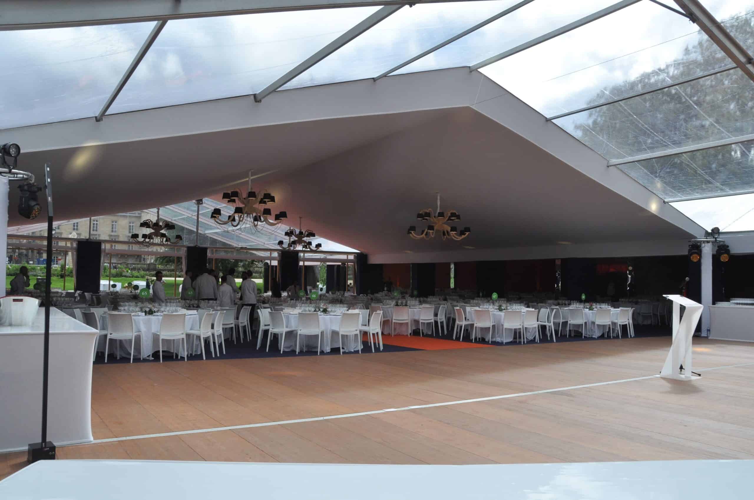Elegant event tent setup with round tables and white chairs for a flower festival.