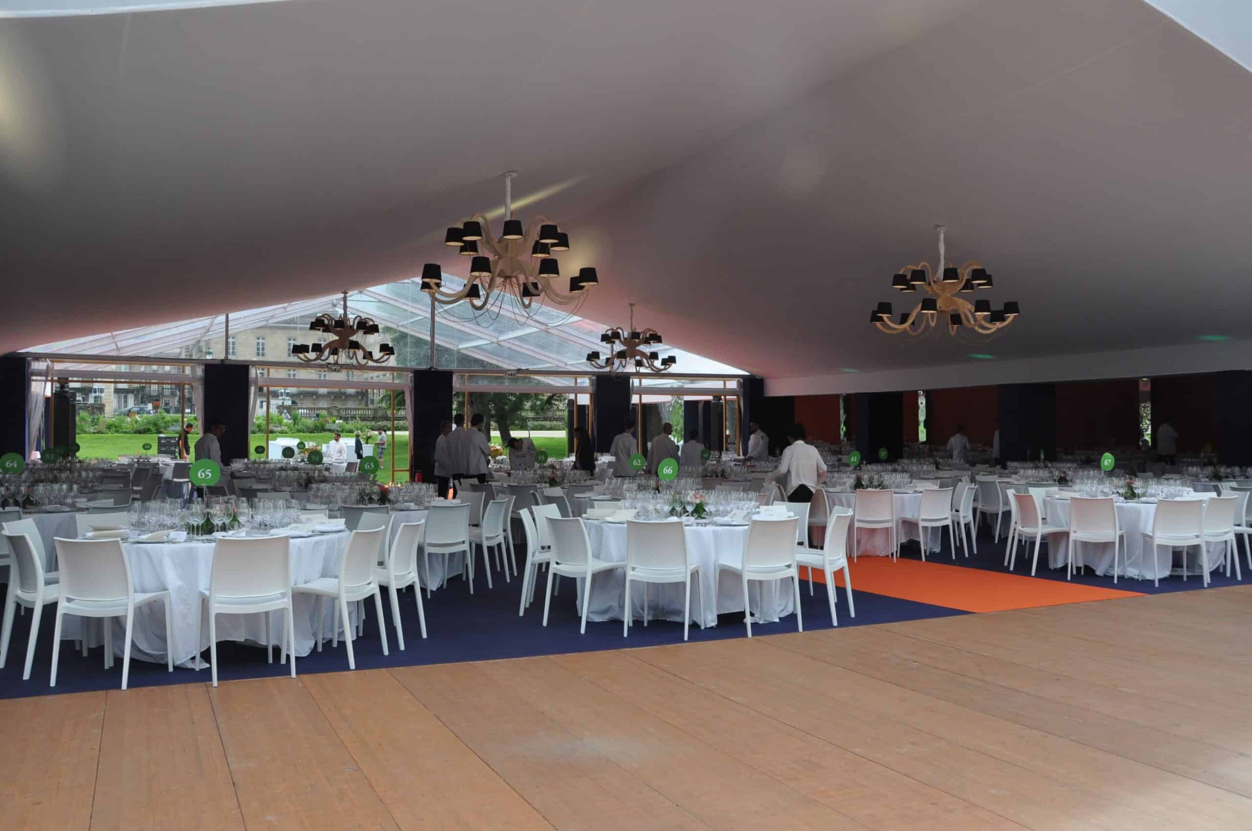 Elegant event setup inside a modern tent with white chairs and tables for a flower festival.