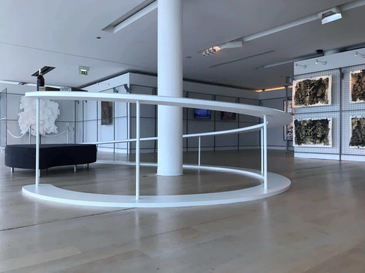 Contemporary art gallery with white curved railing and artwork displays.
