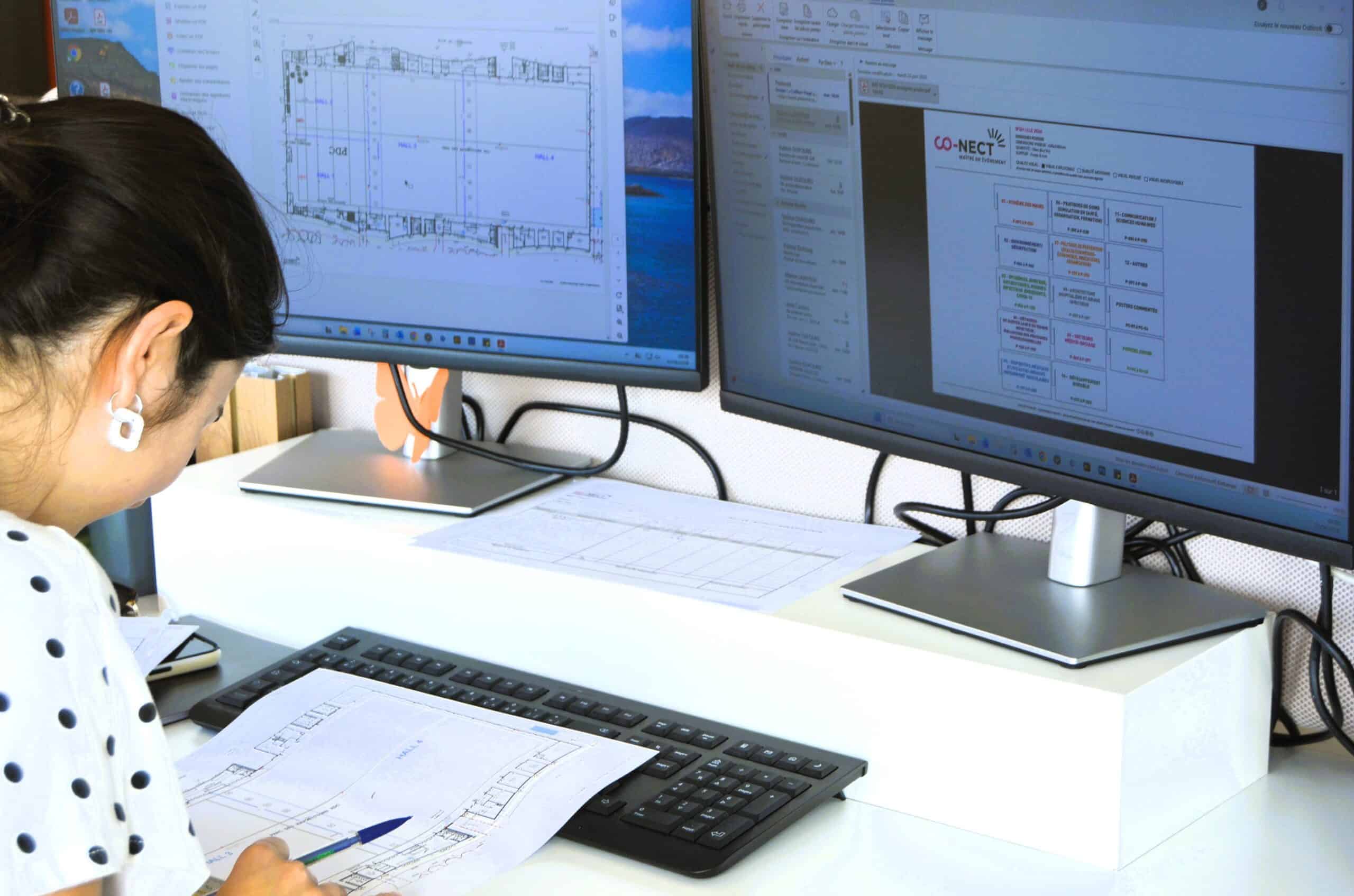 Professional woman working on architectural plans at dual monitors.