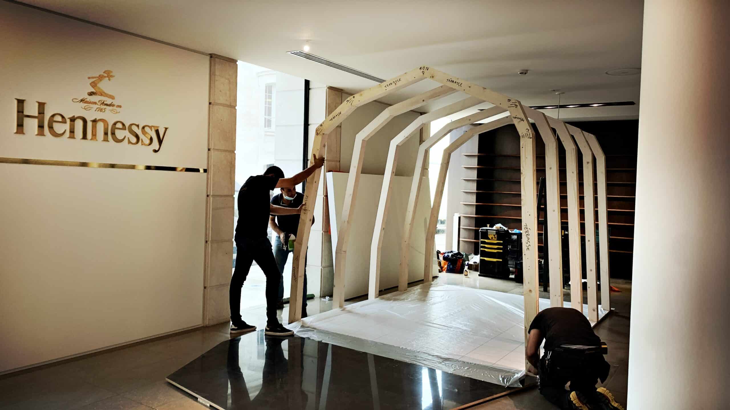 Workers assembling a wooden structure inside a modern office space.