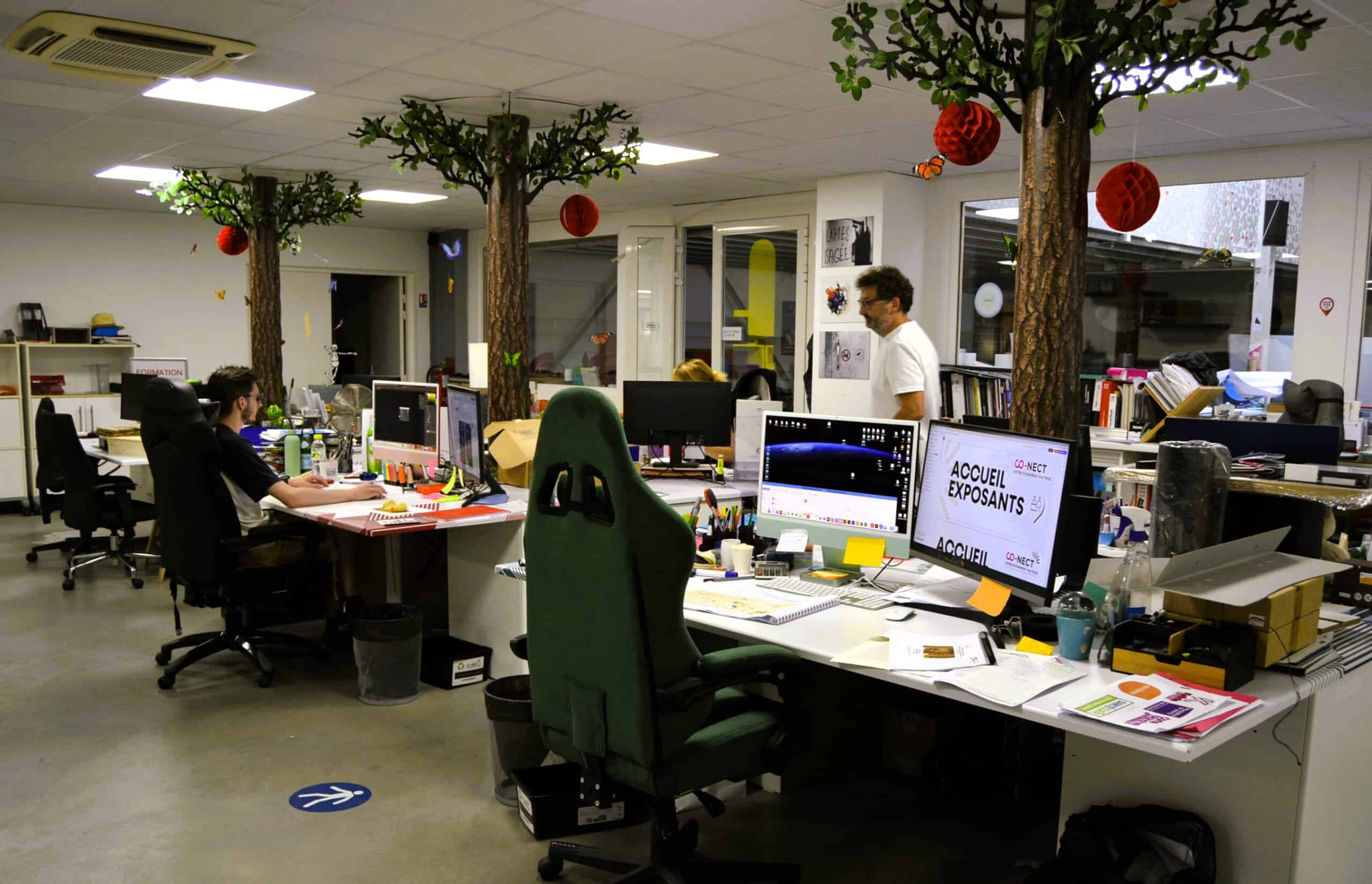 Open-plan office with desks, computers, and decorative trees with red ornaments.