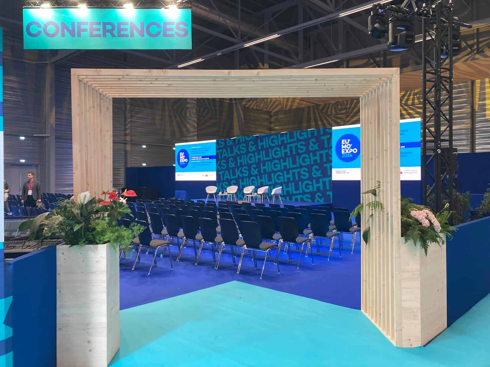 Conference stage with seating and presentation screens at EUMO event.