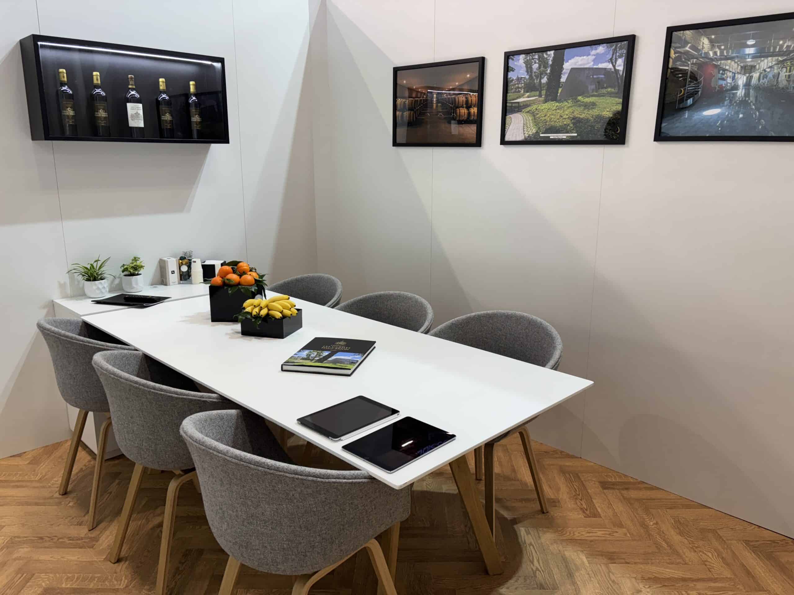 Modern meeting room with white table, gray chairs, and wall-mounted screens.
