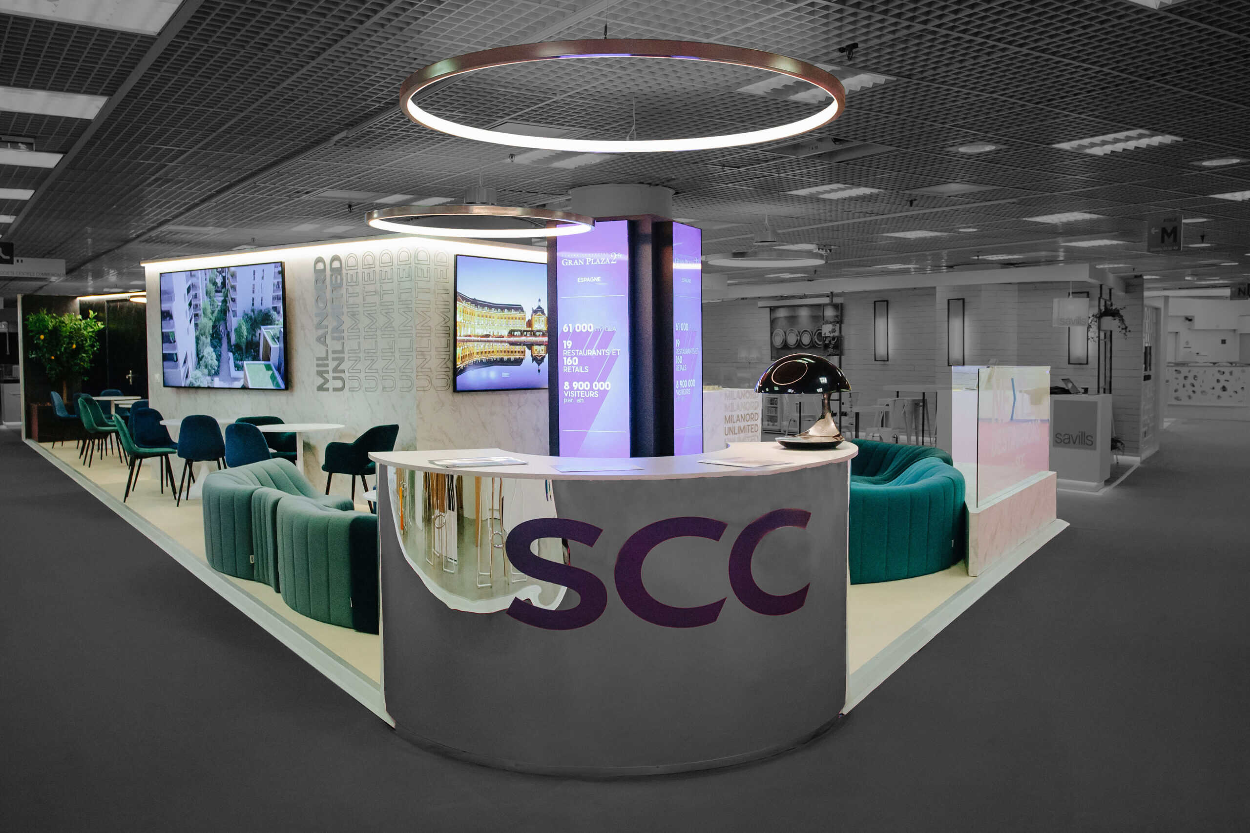 Modern SCC exhibition booth with seating and digital displays at conference.
