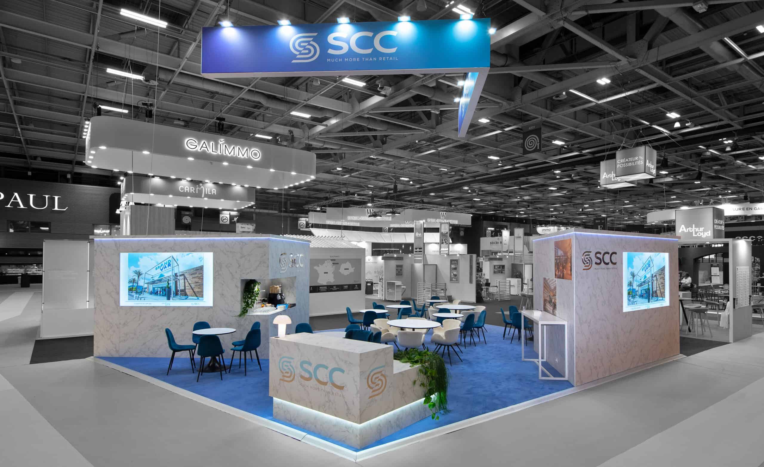 SCC trade show booth with seating and digital displays at an industry event.